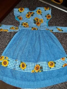 a blue dress with sunflowers and gingham on it sitting on the floor