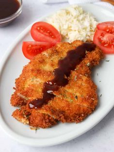 a white plate topped with fried chicken and rice covered in ketchup next to tomatoes