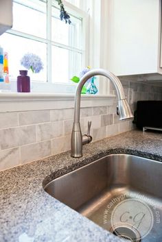 a stainless steel sink in a kitchen with granite counter tops and white cabinetry next to a window