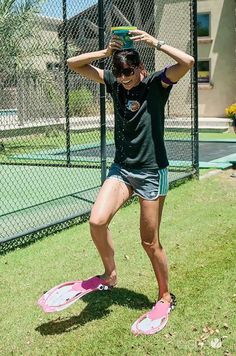 a woman standing on top of a pink skateboard next to a tennis court with her hands behind her head