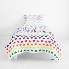 a white bed with multicolored hearts on the cover and pillow cases in different colors