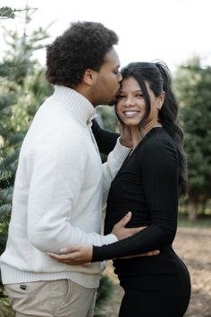 a man and woman standing next to each other in front of a christmas tree farm