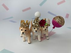 three small dogs wearing crowns and holding balloons