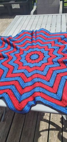 a red, white and blue afghan sitting on top of a wooden table next to a picnic table