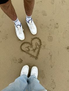 two people are standing in the sand with their feet in the sand and one is drawing a heart