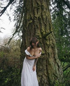 a woman in a white dress standing next to a tree