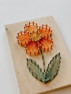 an orange flower made out of string on top of a piece of wood with beads