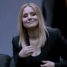 a woman in a black suit is smiling and holding her hands out to the side