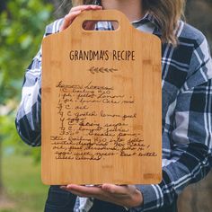 a woman holding up a wooden cutting board with writing on it and the words grandma's recipe written in cursive handwriting