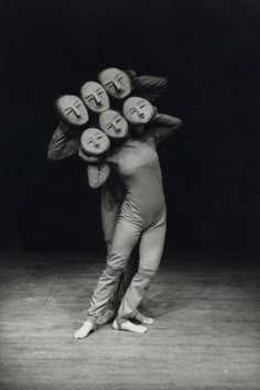 a man is holding several faces on his head while standing in front of a black background