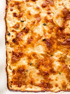 a square casserole dish with cheese and meat toppings, on a white surface