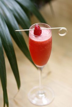 a glass filled with red liquid and topped with a raspberries garnish