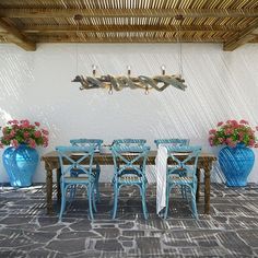 a dining room table with blue chairs under a wooden roof and flowers in vases