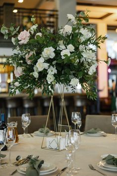 there is a vase with white flowers on top of the table in front of wine glasses