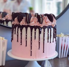 a pink and white cake with chocolate cookies on top is sitting in front of a mirror