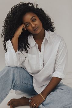 a woman sitting on the ground wearing jeans and a white shirt