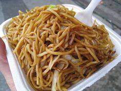 a person holding up a paper container filled with noodles