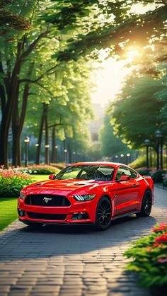 a red mustang parked on the side of a road in front of trees and flowers