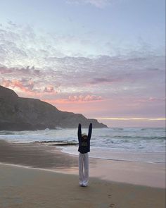 a person standing on the beach with their arms in the air and hands up to the sky