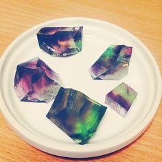 four different colored rocks on a white plate sitting on a wooden table next to a cup and saucer