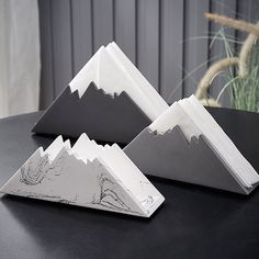 three folded books are sitting on a table with mountains in the background and grass behind them