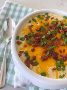 a white bowl filled with soup and topped with bacon, cheese and green onions next to a fork