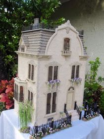 a doll house sitting on top of a table next to flowers and plants in front of it