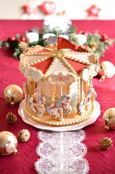 a decorated carousel cake sitting on top of a table next to christmas ornaments and decorations