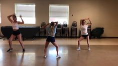 three young women are practicing their moves in a dance studio with chairs and windows behind them