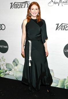 a woman in a black dress posing for a photo on the red carpet at an event