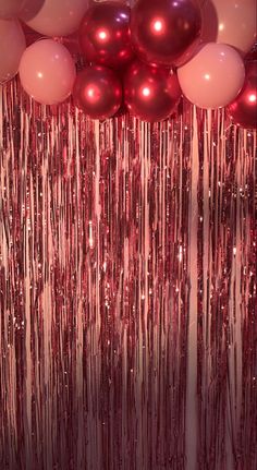 balloons and streamers are hanging in front of a curtain that has pink and red balls on it