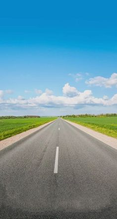 an empty road with grass and blue sky in the background