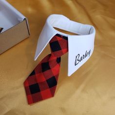 a red and black tie sitting on top of a bed next to an empty box