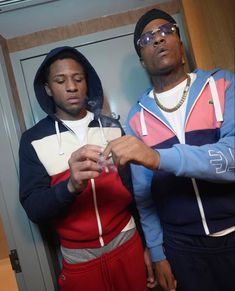 two young men standing next to each other looking at something in their hand while wearing hoodies