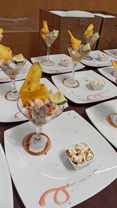 a table topped with white plates filled with desserts and fruit cups covered in toppings