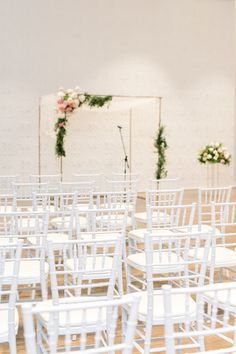 rows of white chairs with flowers and greenery on the wall behind them at a wedding ceremony