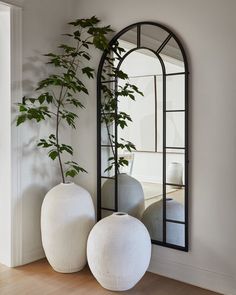 two white vases sitting on top of a wooden floor next to a large mirror