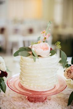 there is a white cake with flowers on the table next to other flowers and greenery