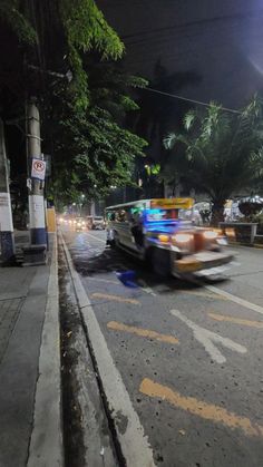 a car driving down the street at night time with lights on and trees in the background