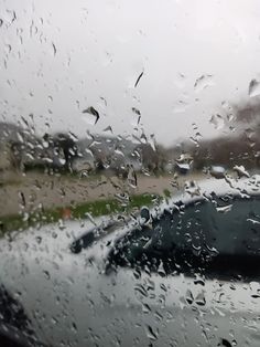 rain drops on the windshield of a car as it drives down a road in the rain