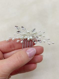 a hand holding a small hair comb with pearls on it's sides and leaves on the top