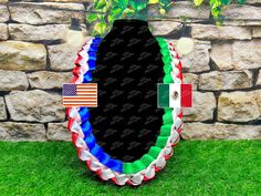 an american and mexican flag wreath on the grass next to a stone wall with flags