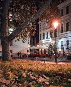 people are sitting at tables under the trees in front of a white building with many windows