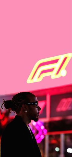 a man with dreadlocks standing in front of a neon sign