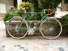 a green and white bicycle parked next to a brick wall in front of some bushes