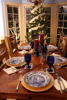 a dining room table set for christmas with blue and white plates, silverware and candles