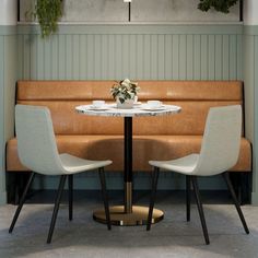 two white chairs sitting at a table in front of a wall with potted plants