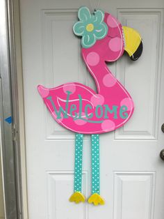 a pink flamingo welcome sign hanging on a door with polka dots and a flower