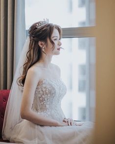 a woman in a wedding dress sitting on a couch next to a window looking out the window