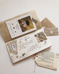 an open book with some pictures on top of it next to papers and envelopes